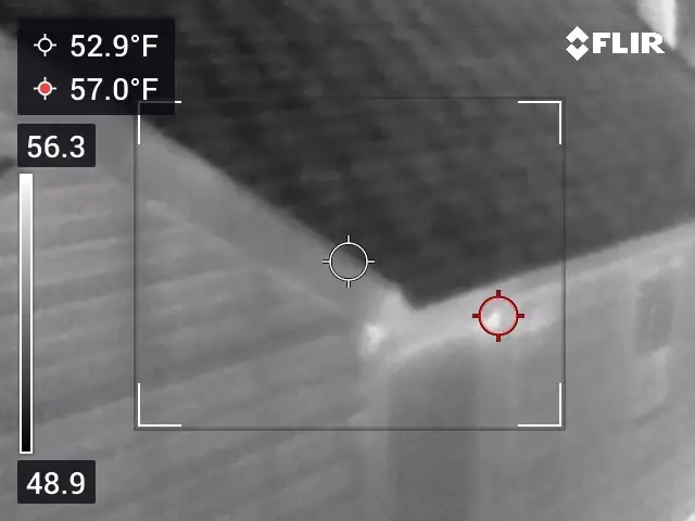 Grayscale thermal image of a roof eave and wall corner with a warmer spot at the corner